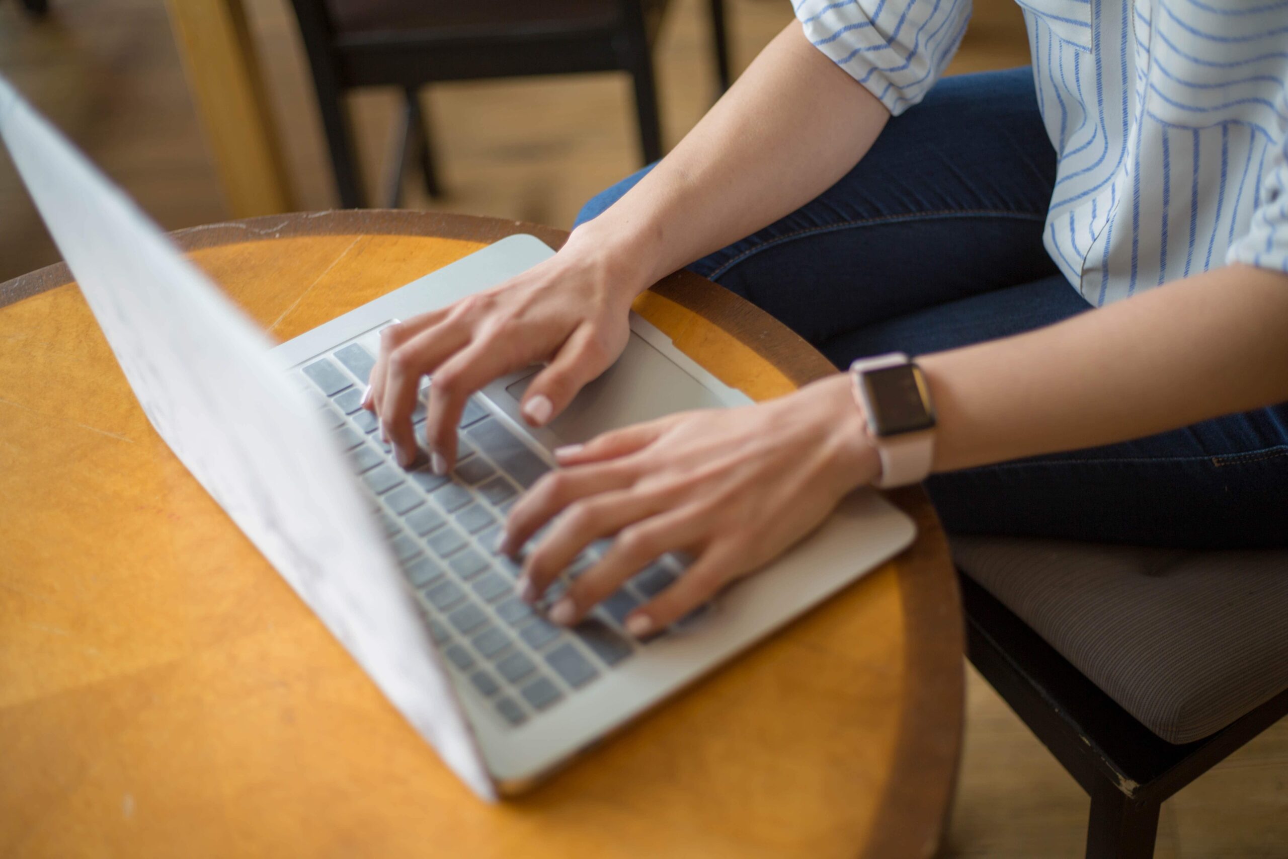 Kobieta pisząca na laptopie, siedząca przy stoliku